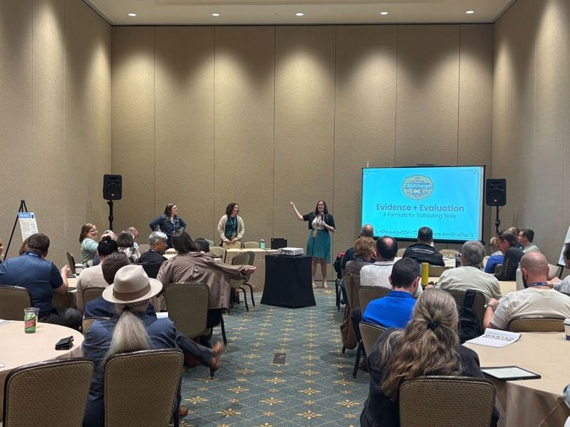 Meghan Raftery presenting at CBExchange 2025, with two co-presenters and a full conference room audience